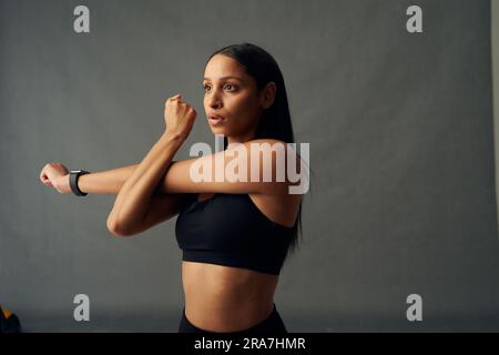 Focused young biracial woman in sports bra doing cross arm stretch in studio Stock Photo