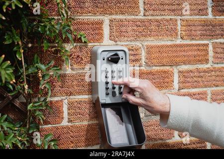 Buttons being pressed by a senior woman on a heavy duty, wall mounted key safe on an exterior brick wall. Stock Photo