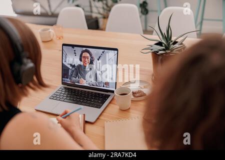 Female student making notes during online lecture while sitting desk in modern coworking Stock Photo