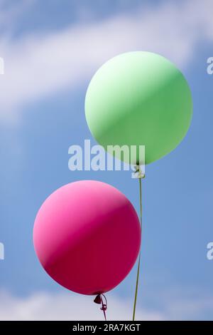 helium inflated green and red balloons flying in the blue sky with clouds Stock Photo