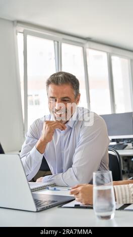 Happy professional mature Latin manager working in office with female colleague. Stock Photo