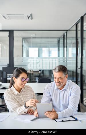 Two diverse business team people talking working using digital tablet in office. Stock Photo
