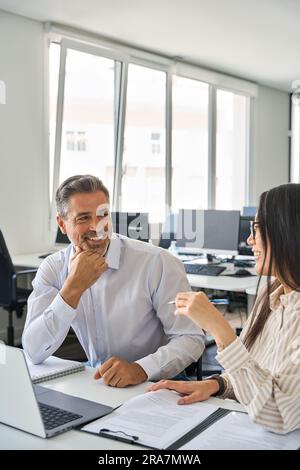 Happy diverse professional workers working in office with laptop, vertical. Stock Photo
