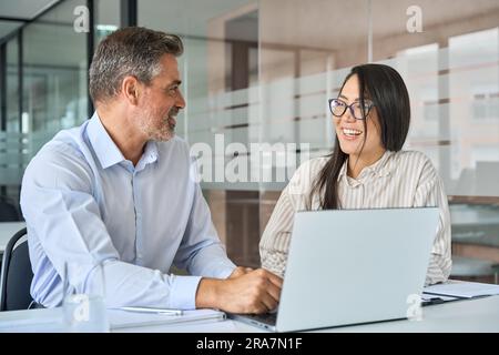 Happy multicultural professionals working in office using laptop, talking. Stock Photo