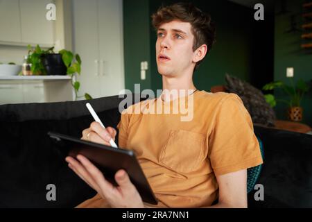 Young caucasian man in casual clothing using digitized pen with digital tablet at home Stock Photo