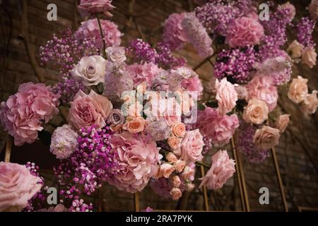 Chivalric wedding with pillars of candles and roses in glass vases. Lush garden arrangements decorating pillars by chairs. Tableware settings + bokeh. Stock Photo