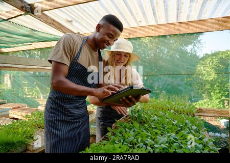 Young multiracial couple wearing aprons smiling while using digital tablet in plant nursery Stock Photo