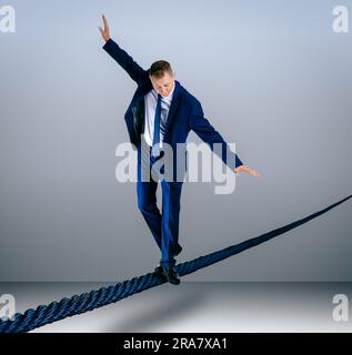 Risks and challenges of entrepreneurship. Businessman balancing on rope against grey background Stock Photo