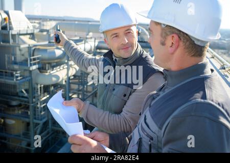 two male workers looking at plans overlooking industrial site Stock Photo