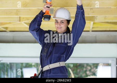 female contractor using a cordless drill on roof timbers Stock Photo