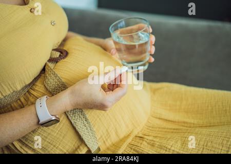 Prenatal Vitamins. Portrait Of Beautiful Smiling Pregnant Woman Holding Supplement and a glass of water, Taking Supplements For Healthy Pregnancy Stock Photo