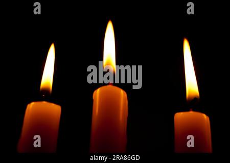 Beautiful image with 3 lighted candles with white and yellowish flames on a black background. Stock Photo