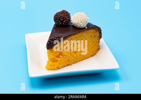 Piece of carrot cake topped with chocolate sauce and brigadeiros (chocolate balls) isolated on blue background. Stock Photo