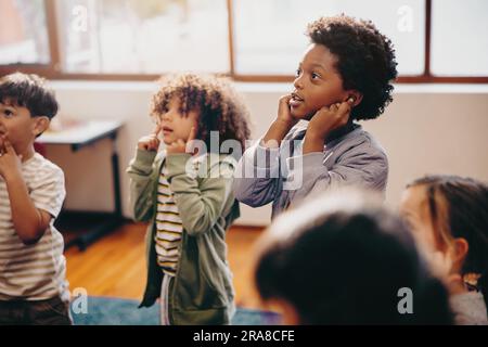 school children learning a nursery rhyme in a class. Group of elementary school kids follow their teacher during a lesson. Early child development in Stock Photo