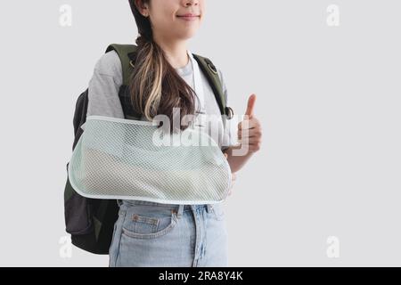 Travel insurance concepts. Young woman with hand injured wearing splint, broken arm, wearing backpack, showing thumb up, smiling face Stock Photo