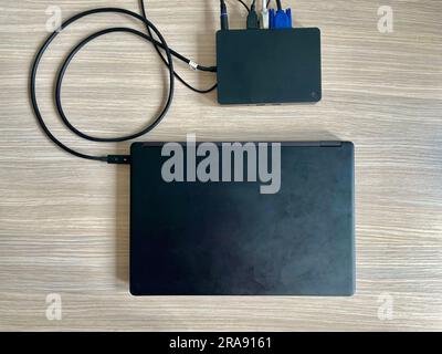 A black laptop connected to a black docking station with a USB cable. Clean office desk. Efficient workstation layout. No logos. Stock Photo