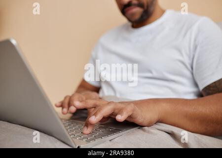 Close up of black man using laptop in bed at home with focus on male hands typing, copy space Stock Photo