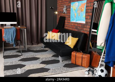 Stylish teenager's room with black sofa, computer, suitcase and world map on brick wall Stock Photo