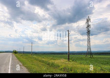 Power transmission towers over a rural field in the countryside. Gloomy sky with clouds. Stock Photo