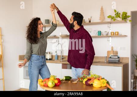 Loving middle eastern couple cooking and having fun, dancing and spending time in kitchen interior at home, free space Stock Photo