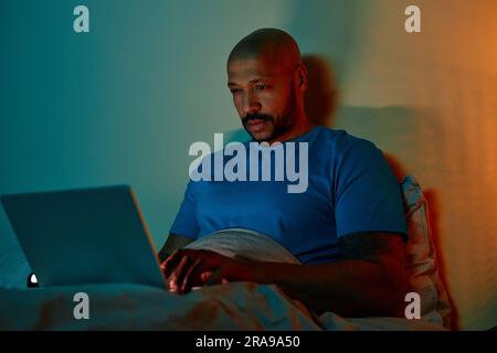 Portrait of adult black man using laptop in bed at night suffering from insomnia Stock Photo