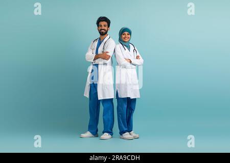 Smiling arab male and female doctors posing in uniform over blue background Stock Photo