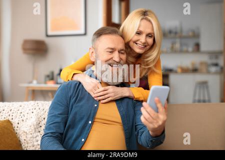 Happy Mature Spouses Using Mobile Phone With Application At Home Stock Photo