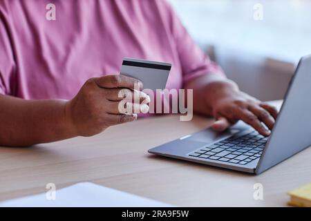 Focus on hand of senior woman with credit card sitting by desk and using laptop while ordering things in online shop and paying for them Stock Photo