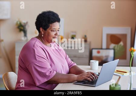 Side view of senior African American businesswoman typing on laptop keyboard while sitting by workplace in home office and networking Stock Photo