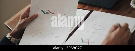 Over the shoulder wide view image of a businesswoman reviewing and reading business sales report documents. Closeup of hands holding the folder with p Stock Photo