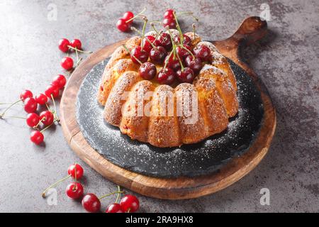 Rustic style cherry cake decorated with fresh berries and powdered sugar close-up on a wooden board on the table. Horizontal Stock Photo