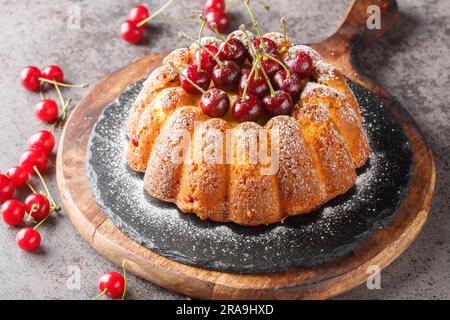 Delicious biscuit vanilla cherry bundt cake decorated with fresh berries and powdered sugar close-up on a wooden board on the table. Horizontal Stock Photo