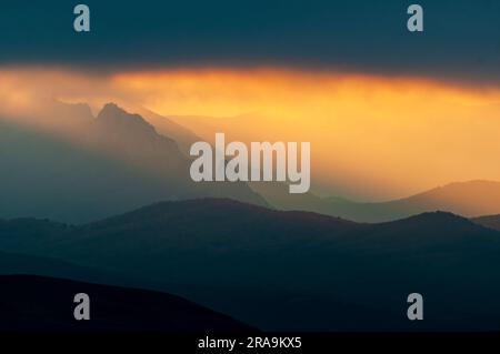 Amazing mountain landscape. Mountain peaks with dramatic low clouds and sun rays shining through the clouds. Stock Photo