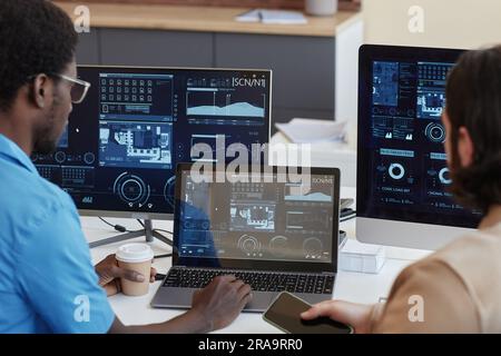 Focus on laptop with statistic graphic data on screen and young African American IT manager and his colleague sitting by workplace Stock Photo