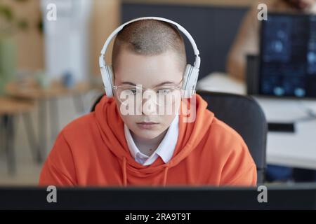 Young serious female analyst in eyeglasses and headphones looking at screen of computer and thinking of how to decode and read information Stock Photo