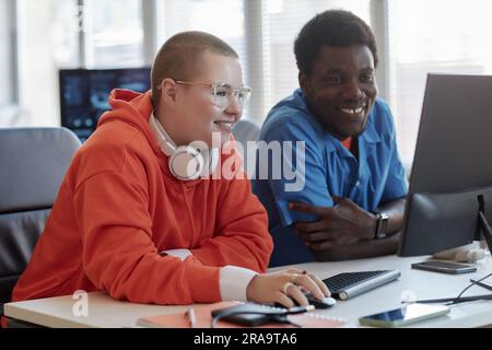 Two happy young intercultural cyber security engineers sitting by workplace in front of computer screen and looking through data Stock Photo