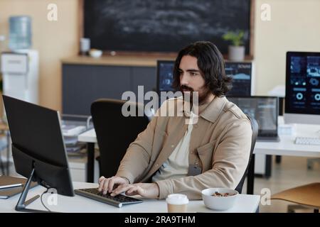 Young serious businessman typing on keyboard and looking at computer screen while analyzing data or creating new algorithms or software Stock Photo