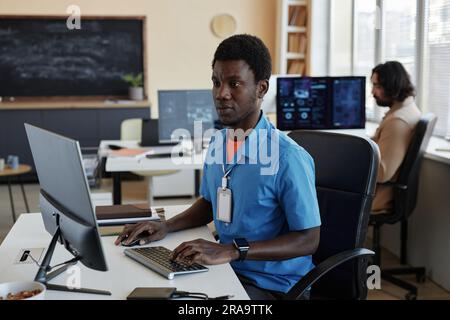 Young serious African American programmer sitting in front of computer monitor, looking at screen and typing while working over new software Stock Photo