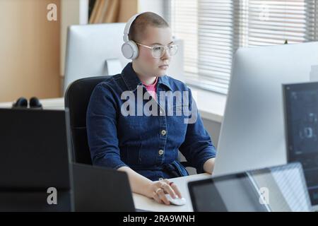 Young serious female cyber security manager clicking computer mouse and looking at screen while learning data or decoding it by workplace Stock Photo