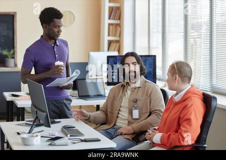 Young confident businessman explaining his viewpoint about new software for decoding data to intercultural colleagues at working meeting Stock Photo
