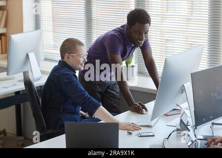 Two happy young intercultural cyber security managers looking at screen of computer while discussing online data or new decoding algorithms Stock Photo