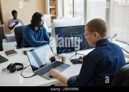 Young female cyber security manager using laptop while sitting by workplace in front of computer screen and working with data Stock Photo