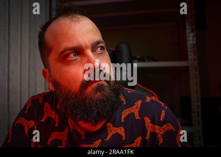 Portrait of an adult male with a beard, works in front of a computer, mixed color light, indoor Stock Photo