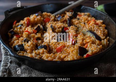 Vegetable rice with mediterranean vegetables such as eggplant, bell peppers, tomatoes, herbs, onions and garlic in cast iron pan Stock Photo
