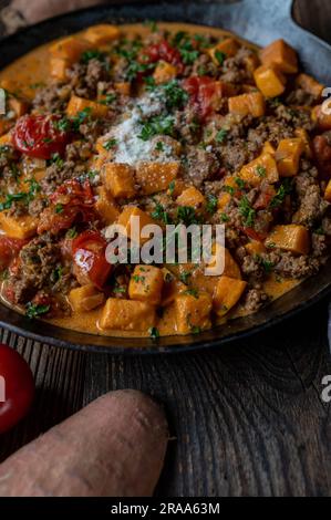 Sweet potato, ground beef with vegetable and parmesan cheese in a cast iron pan Stock Photo