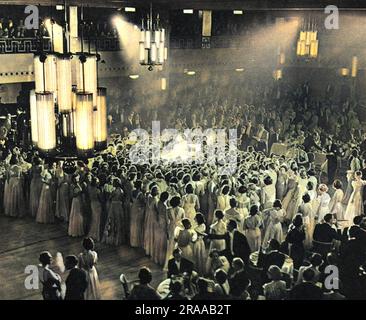 A huge white cloud of debutantes around the traditional huge cake wheeled out at Queen Charlotte's Ball and cut by the guest of honour, in the case of this year, the Duchess of Gloucester.  Queen Charlotte's Ball, held in honour of the wife of King George III and revived in 1925 to raise funds for the maternity hospital of the same name was one of the highlights of the London Season for a debutante.  All the girls would be dressed in white, and would dip into a carefully choreographed curtsy as the cake was cut which was lit by candles representing the number of years since the Queen's birth. Stock Photo