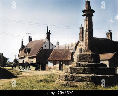 A corner of Great Brington village, Northamptonshire, England, with its thatched stone cottages and ancient cross.     Date: 1950s Stock Photo