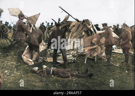 A crashed British plane with the dead pilot lying on the ground during the First World War.  German soldiers gather round to examine the wreckage.     Date: 1914-1918 Stock Photo