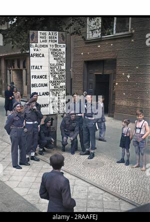 Street scene in Berlin, Germany, at the end of the Second World War, with soldiers and children.  A sign reads: This Axis has been laid from El Alamein to Berlin via Africa, Italy, France, Belgium, Holland, Germany, with various place names listed.     Date: 1945 Stock Photo