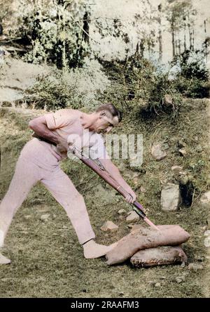 Soldier in side view, stabbing a stuffed sack with a bayoneted rifle, India.     Date: 1918 Stock Photo